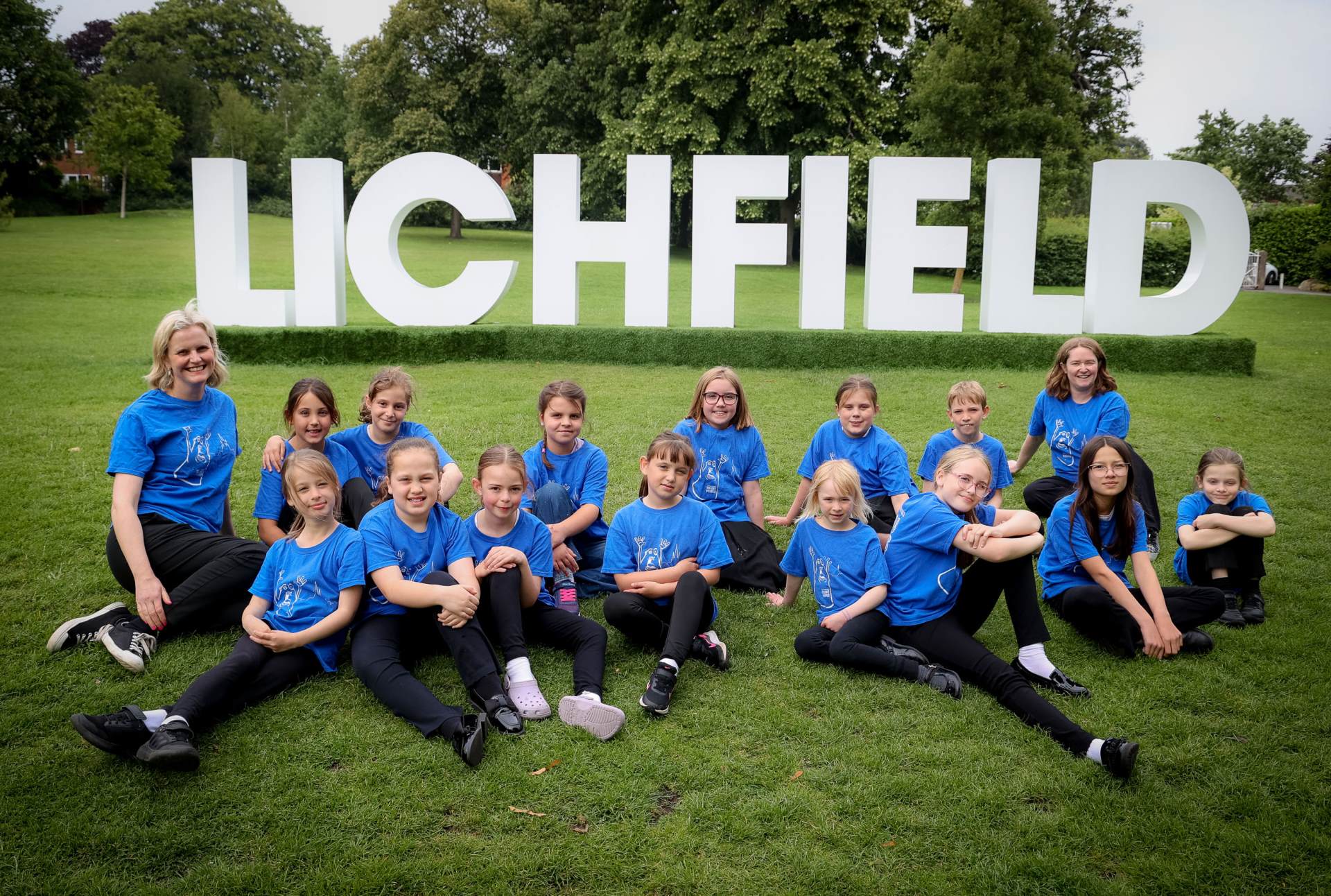 Young Voices 2025 Young Voices choir sitting in front of Lichfield sign